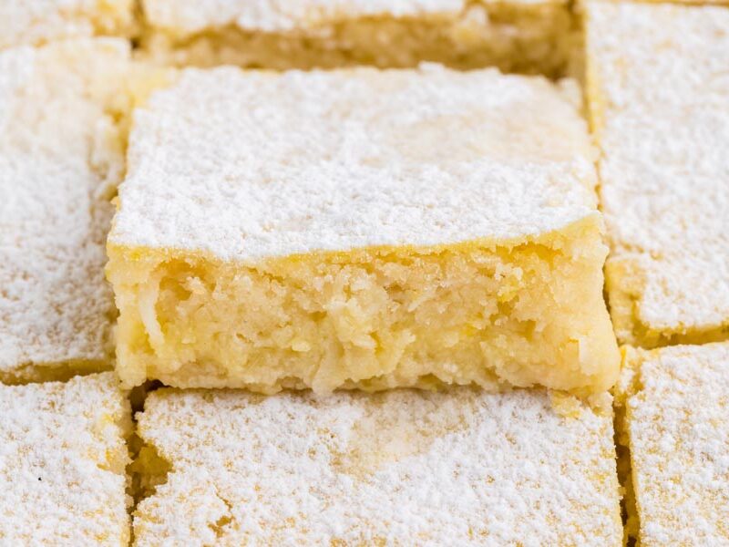 A lemon bar topped with powder sweetener popping out of the row of other bars.