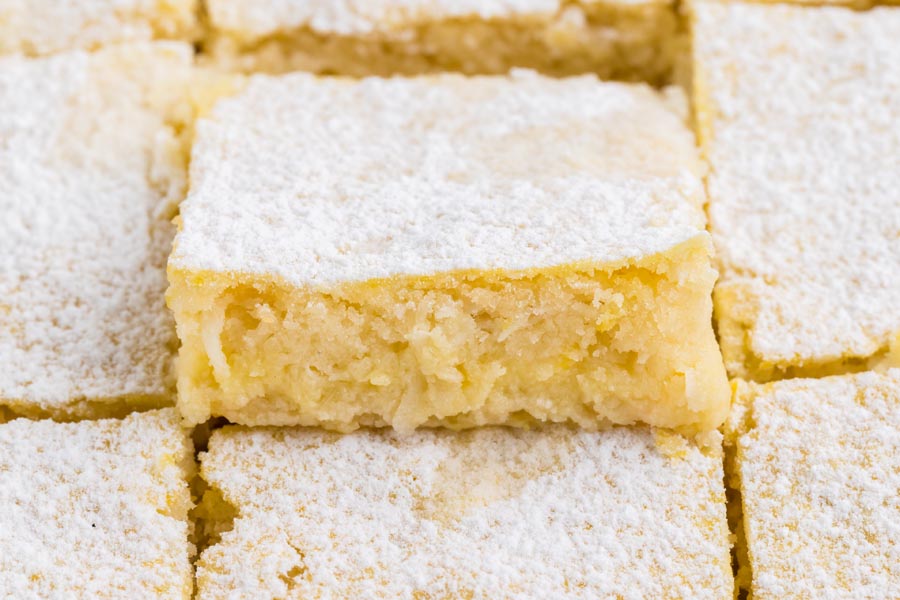 A lemon bar topped with powder sweetener popping out of the row of other bars.