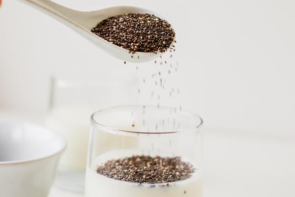 pouring a tablespoon of chia seeds into glass of nut milk