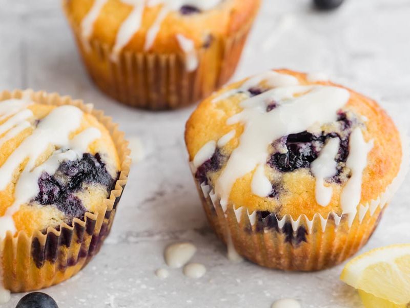 three keto lemon flavored muffins with blueberries inside wrapped in a muffin liner
