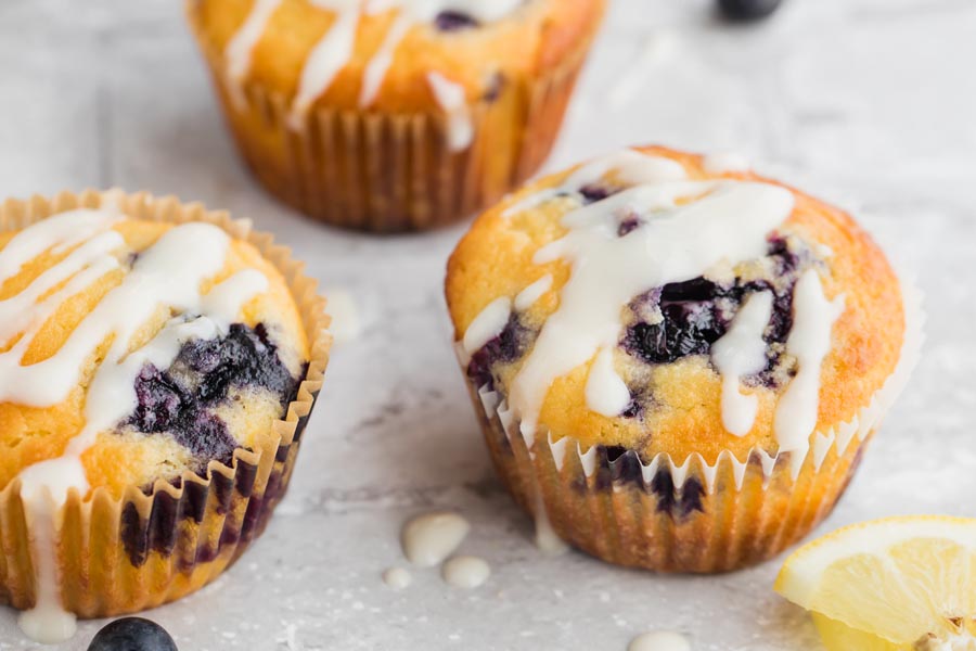 three keto lemon flavored muffins with blueberries inside wrapped in a muffin liner