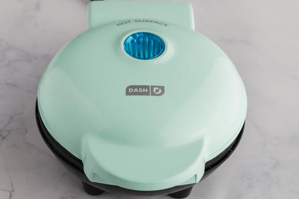 teal chaffle waffle maker sitting on a counter all lonely and by itself