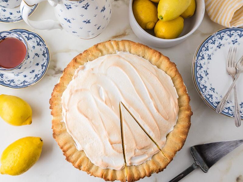 Keto lemon meringue pie with lemons, teacups and blue-and-white plates.