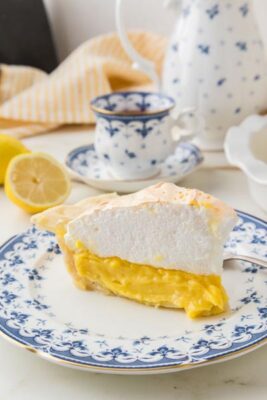 Side view of a keto lemon meringue pie slice featuring layers of buttery crust, tangy lemon curd, and tall toasted meringue.