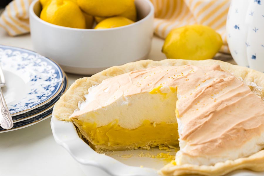 Whole keto lemon meringue pie with a slice removed, revealing the bright lemon filling beneath a thick layer of lightly toasted meringue.