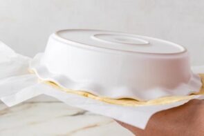 Keto pie dough being flipped out onto parchment paper using an inverted pie dish.