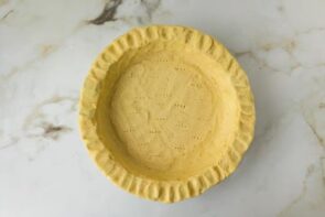Unbaked keto pie crust pressed into a pie plate and docked with a fork before baking.