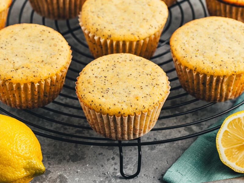 A bunch of baked lemon poppyseed muffins on a black wire rack.