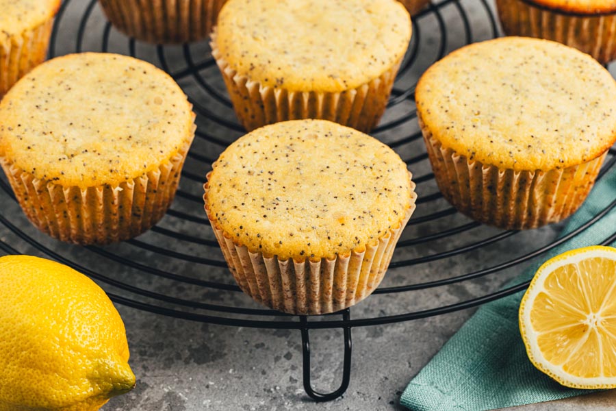 A bunch of baked lemon poppyseed muffins on a black wire rack.