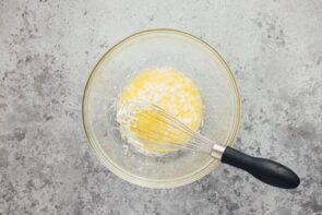 Melted butter and oil in a glass dish with a whisk over it.