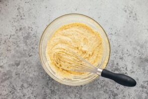 Poppyseed muffin batter in a bowl with a black handled whisk.