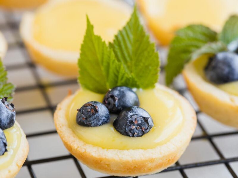 Mini keto lemon tart topped with blueberries and mint on a cooling rack.