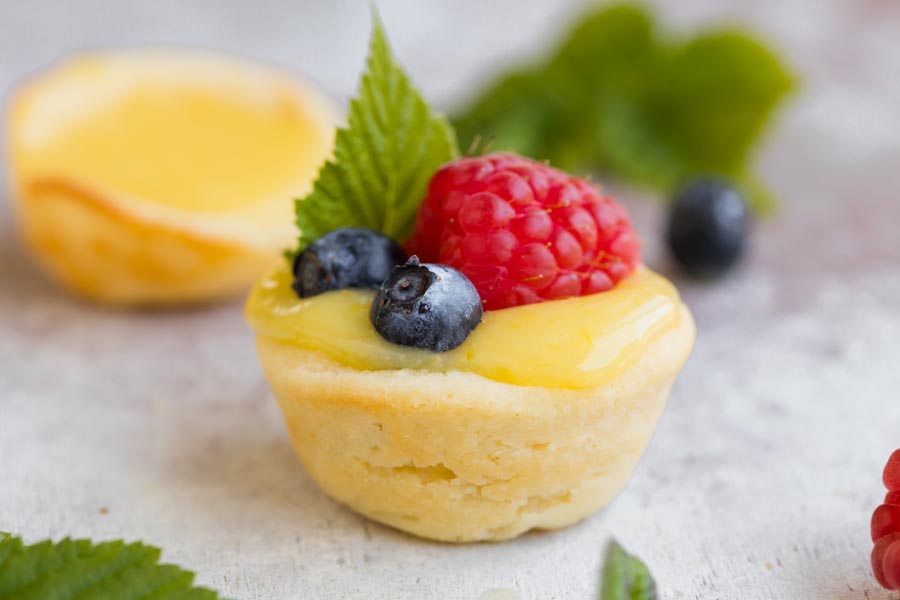 A close up of the flaky crust surrounding a lemon tart topped with berries.