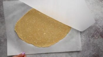 Peeling back parchment paper to reveal pie crust with chunks of butter in the dough.