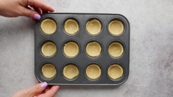 Holding onto a muffin pan filled with mini unbaked pie crusts.
