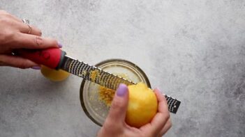 Hands zesting a lemon with a zester.