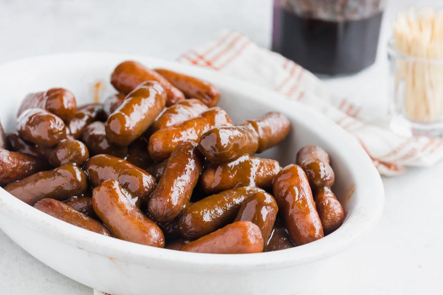 A bowl of cocktail weenies tossed in bbq sauce and grape jelly with toothpicks in the background.