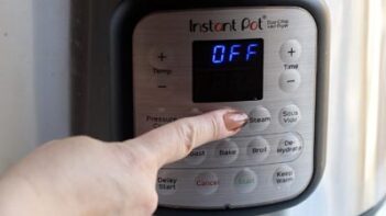A finger pressing the start button on an Instant Pot.
