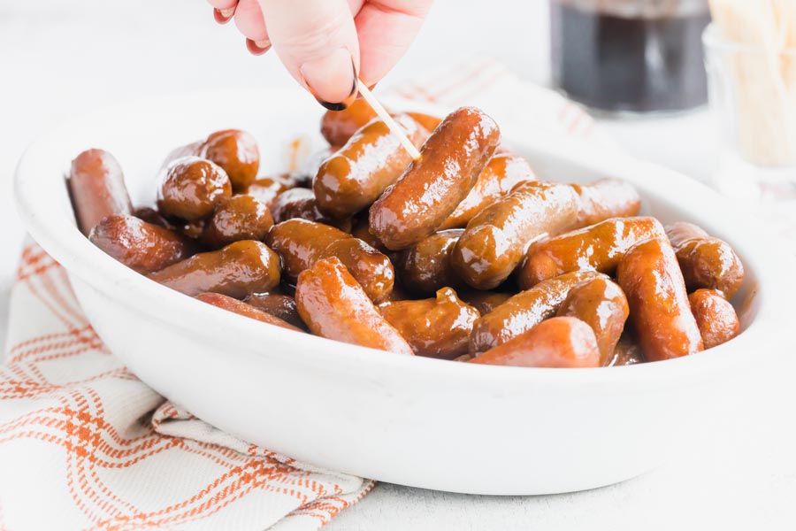 A toothpick holding a lit'l smokie sausage over a bowl.