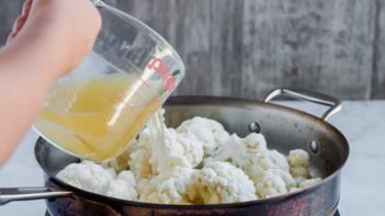 pouring chicken broth into a skillet with caulilower florets