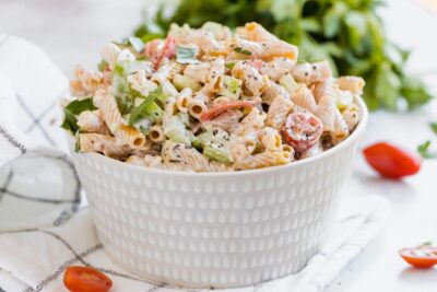a beige bowl with macaroni salad mixed with celery and tomatoes