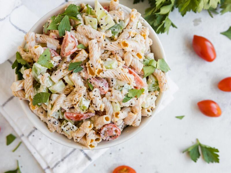 a bowl of pasta salad near tomatoes and parsley leaves