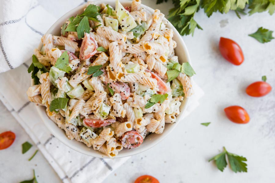 a bowl of pasta salad near tomatoes and parsley leaves