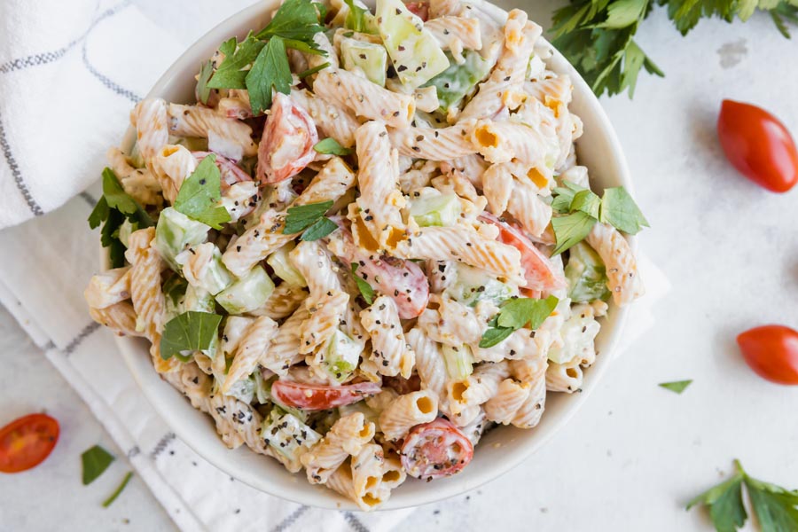 looking down into a bowl filled with macaroni pasta salad with celery, parsley and tomatoes and topped with black pepper