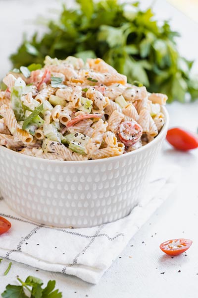 a bowl filled with macaroni salad with sliced tomatoes near by