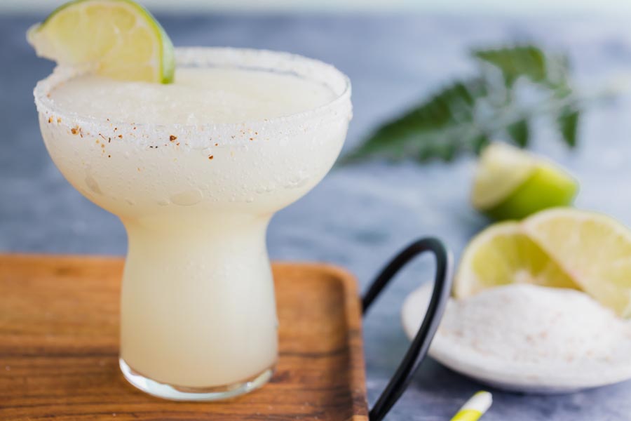 a margarita in a salted glass with salt and more lime wedges nearby