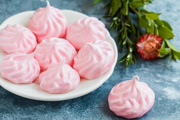 pink meringue cookies on a white plate with flowers near