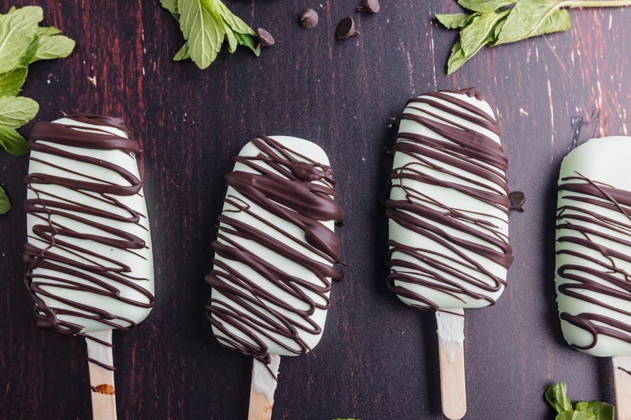 four mint ice cream bars on a dark surface drizzle with chocolate