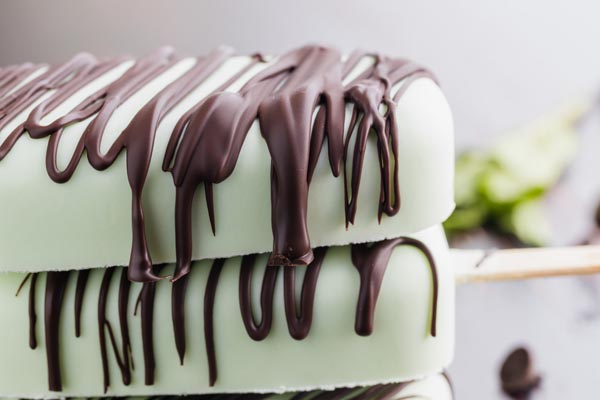 close up of light green mint popsicles drizzled with chocolate stacked