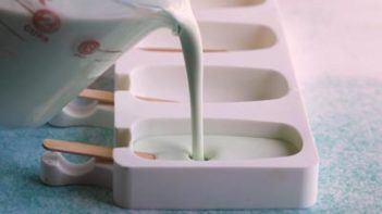 pouring green mint ice cream mixture into popsicle molds