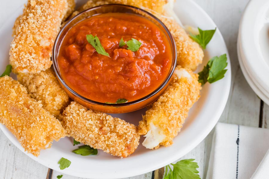 a big plate of crispy pork rind coated cheese sticks with a dish of pizza sauce inside