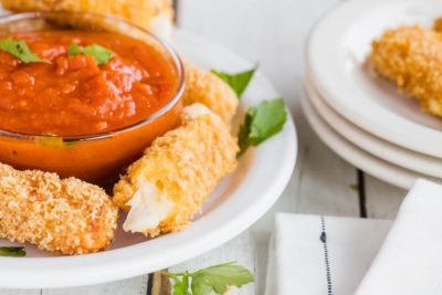 mozzarella cheese sticks on a white plate with marinara sauce and parsley flakes
