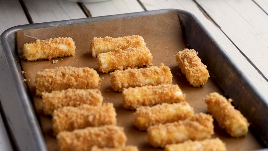 crispy coated cheese sticks on a baking sheet