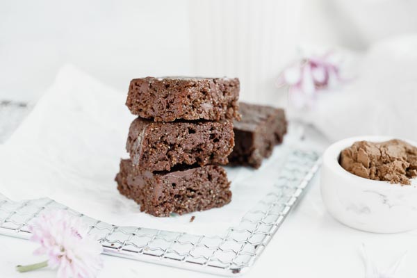 brownies sitting on a white rack with cocoa powder near by