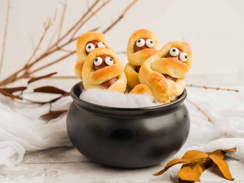 four creepy keto mummy dogs in a black calderon with twigs behind it