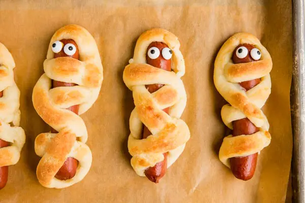 three hot dogs wrapped like a mummy with candy eyeballs