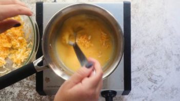 whisking in shredded cheese into a saucepan