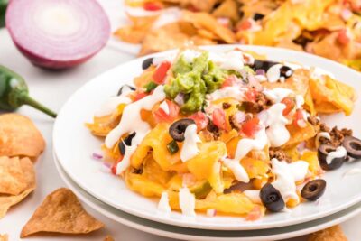 A plate of cheesy keto nachos topped with sour cream, olives, guacamole and pico de gallo.