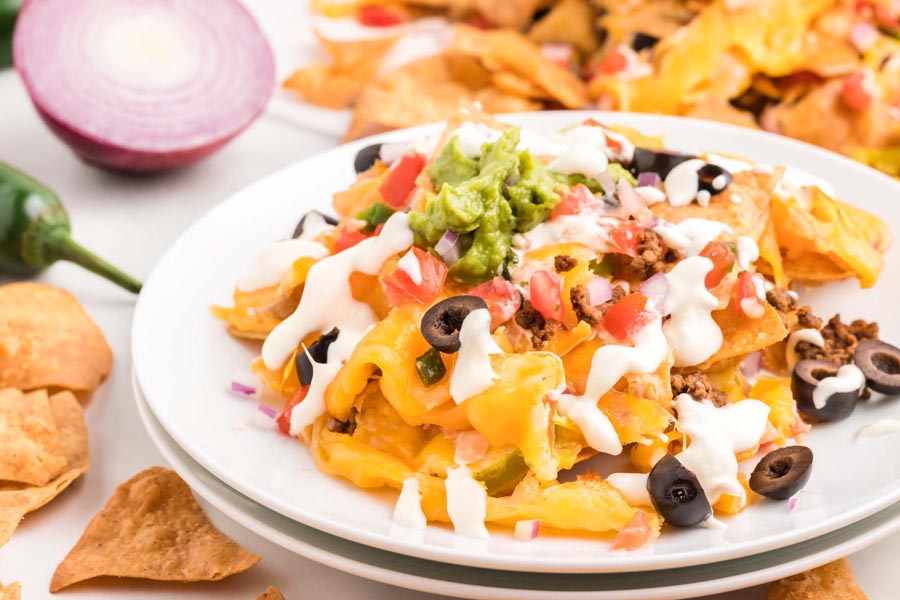 A plate of cheesy keto nachos topped with sour cream, olives, guacamole and pico de gallo.