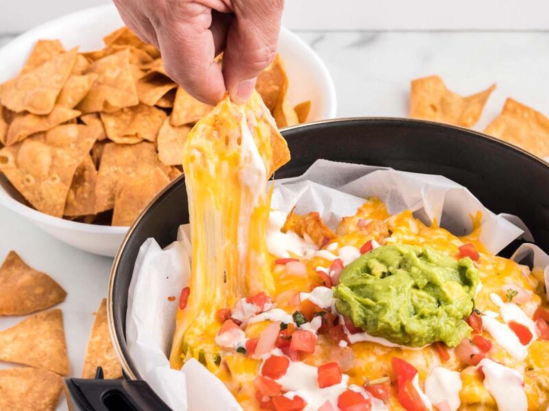 A hand pulling a chip covered in cheese while the cheese pulls away.