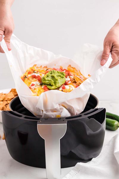 Hands pulling out a pile of nachos from a sheet of parchment paper.