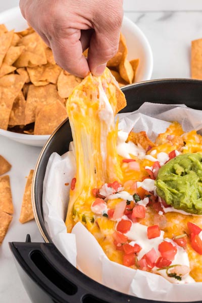 A hand pulling a cheese covered tortilla chip out of a pile of nachos.