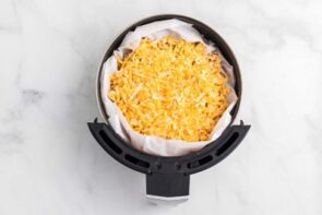 An air fryer basket filled with cheese topped nachos.