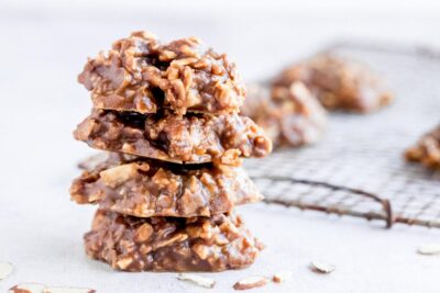 A stack of four no bake chocolate cookies next to slices almonds.