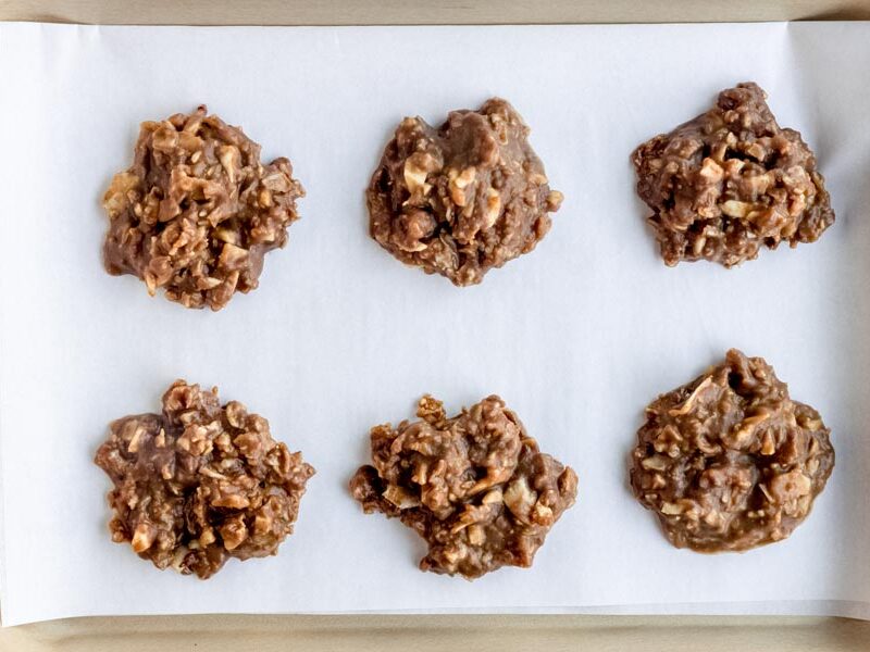 Six chocolate no bake keto cookies on a parchment lined baking tray.