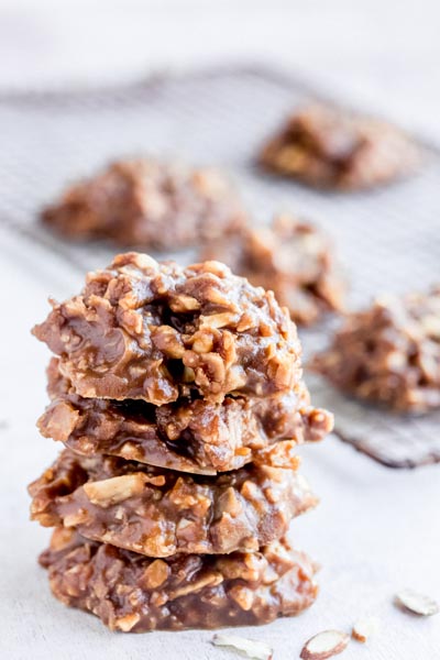 A stack of no-bake cookies in front of a more cookies sitting on a wire cooling rack.